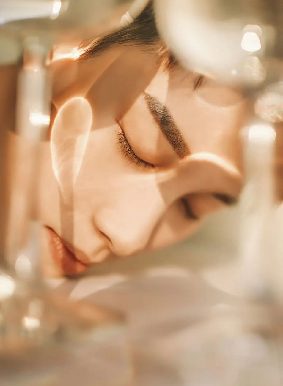 Close-up of a woman's face with eyes closed, seen through glass in warm light
